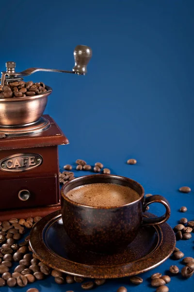 Copo com café e moedor de café manual com grãos de café em um fundo azul. — Fotografia de Stock