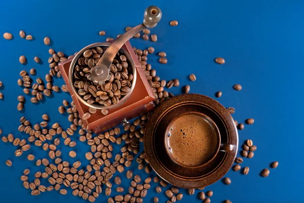 Filiżanka z kawą i ręcznym młynkiem do kawy z ziarnem kawy na niebieskim tle. Układy płaskie. — Zdjęcie stockowe