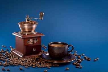 Kahve fincanı ve kahve değirmeni ile mavi arka planda kahve çekirdekleri..