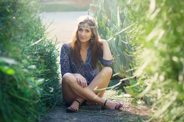 Chica hippie sentado en el suelo en el parque con arbustos verdes —  Fotos de Stock