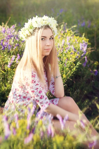 Menina loira com coronet flor sentado no campo com flores — Fotografia de Stock