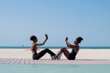 Afrika kökenli iki kadın deniz kenarında oturuyor ve Dubai plajında birlikte spor egzersizleri yapıyor, Bae