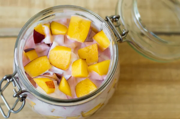 Rebanadas de fruta fresca mezcladas con yogur en un recipiente de vidrio para alimentos. Concepto de alimentación saludable. Concepto de almacenamiento de alimentos — Foto de Stock
