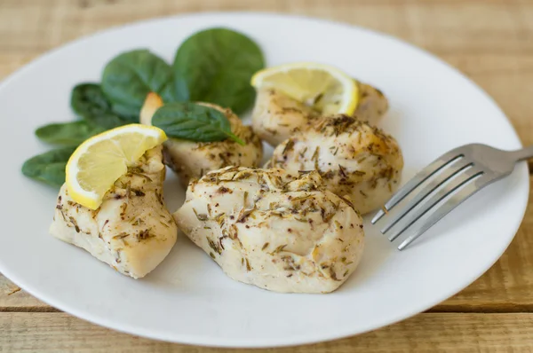 Filet de poulet cuit au four avec tranches de citron et feuilles d'épinards sur une assiette simple blanche — Photo