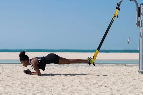 Africana haciendo ejercicios difíciles usando cuerdas especiales para el entrenamiento en suspensión. Actividad deportiva en la playa de Dubai, Emiratos Árabes Unidos —  Fotos de Stock