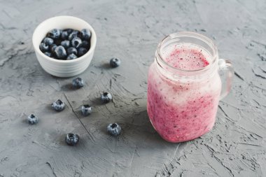 İçme bardağında yabanmersini püresi ve beton arkaplanda taze böğürtlenlerle dolu küçük bir kase.