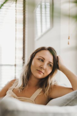 Evdeki kanepede oturan genç bir kadının portresi. Sıradan bir görünüm. Evdeki rahatlık ve rahatlık. Evde dinleniyorum.