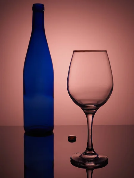 Renkli arka planda bir şişe şarap ve boş şarap kadehi yansımaları ve bir bardak damlası..