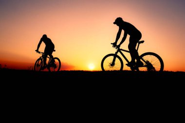 Gün batımında yolda bisikletçilerin siluetleri.