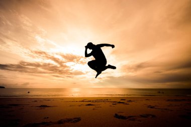 Sahilde zıplayan bir adamın silueti.