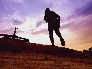 Bir dağ bisikletçisinin silueti Akşamları yüksek bir dağda, Pastel gökyüzü ile dinleniyor.