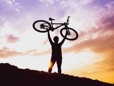 Bir dağ bisikletçisinin silueti Akşamları yüksek bir dağda, Pastel gökyüzü ile dinleniyor.