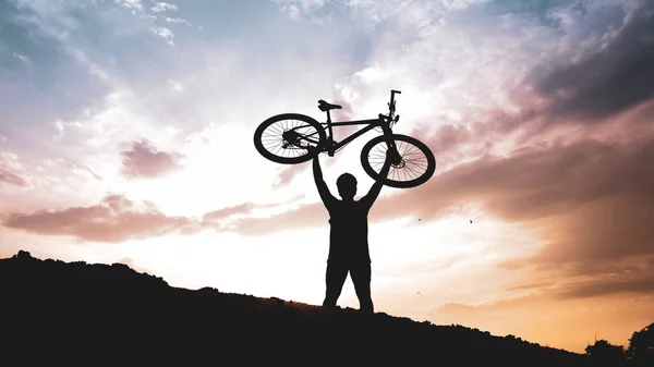 The mountain biker's silhouette lifts the bike happily that he has succeeded. from the competition On the high mountains in the evening, it is colorful.