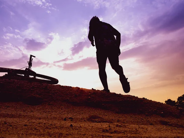 Bir dağ bisikletçisinin silueti Akşamları yüksek bir dağda, Pastel gökyüzü ile dinleniyor.
