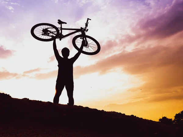 The mountain biker\'s silhouette lifts the bike happily that he has succeeded. from the competition On the high mountains in the evening, it is colorful.