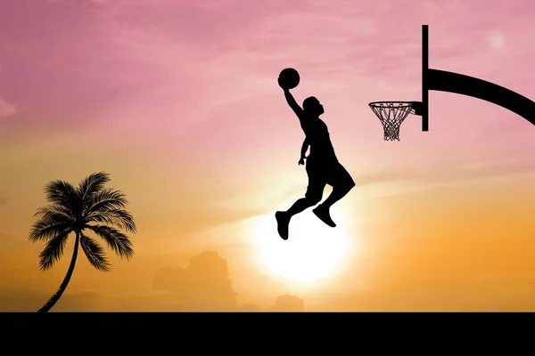 Basketball players jumping dunk silhouettes on a beautiful outdoor basketball court in the evening.