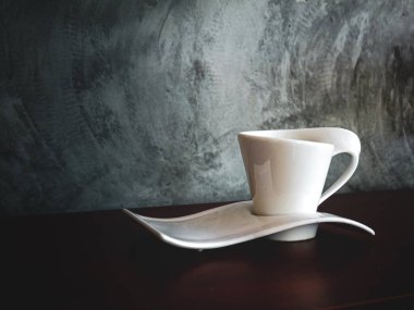 Gri alçı duvarlı arka planda güzel renkli bir kahve fincanı bir masanın üzerine konur..