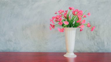 Masanın üzerine bir vazo kırmızı çiçek, alçı bir duvarın arka planına yerleştirilir..