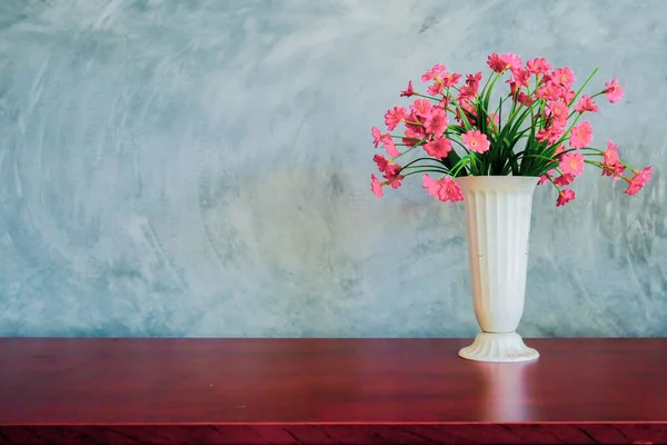 A vase of red flowers is placed on the table against a backdrop of a plaster wall.