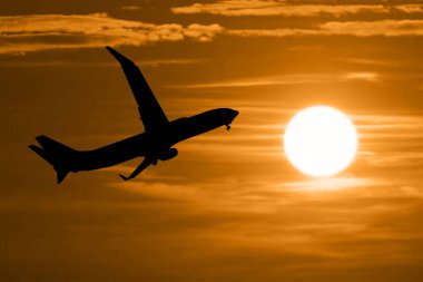 Akşam havaalanından kalkan yolcu uçağının silüeti. Arka planda güneş var.