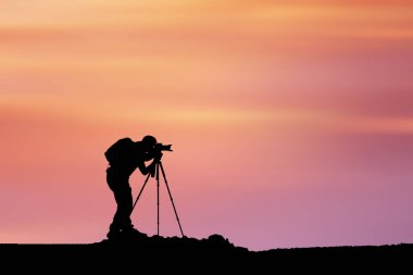 Gün batımında arka planda kamera olan bir fotoğrafçının silueti.