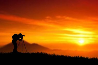 Gün batımında arka planda kamera olan bir fotoğrafçının silueti.