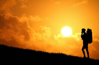 Sırt çantasının silueti tepenin üstünde duruyor ve arka planda günbatımı gökyüzü var