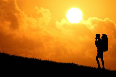 Sırt çantasının silueti tepenin üstünde duruyor ve arka planda günbatımı gökyüzü var