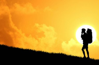 Sırt çantasının silueti tepenin üstünde duruyor ve arka planda günbatımı gökyüzü var