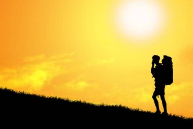 Sırt çantasının silueti tepenin üstünde duruyor ve arka planda günbatımı gökyüzü var