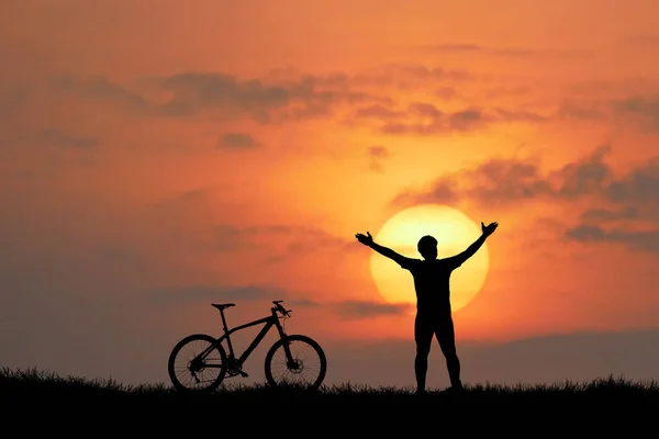 背景には夕焼け空の男と自転車のシルエット — ストック写真