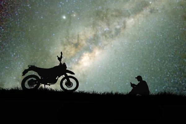 silhouettes of man and bike on hilltop with stars in sky