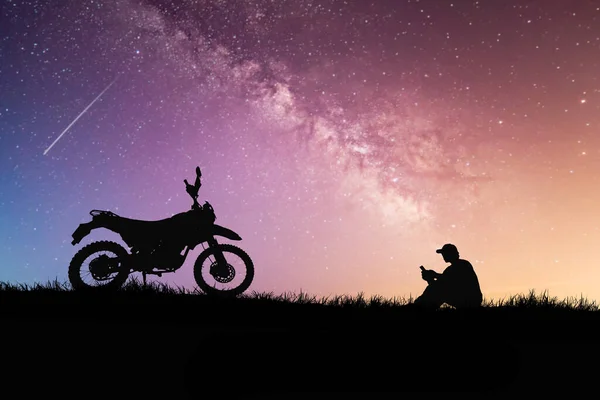 silhouettes of man and bike on hilltop with stars in sky