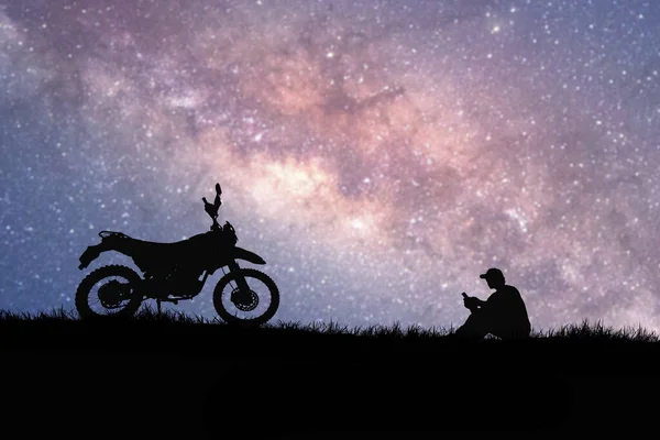 silhouettes of man and bike on hilltop with stars in sky