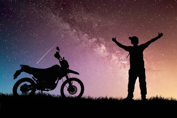 silhouettes of man and bike on hilltop with stars in sky