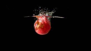 Kırmızı elma siyah arkaplanda suya düşüyor.