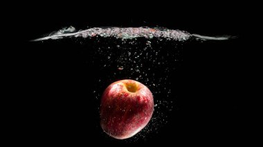 Kırmızı elma siyah arkaplanda suya düşüyor.