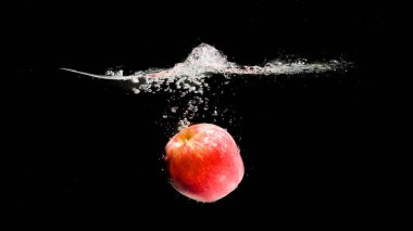 Kırmızı elma siyah arkaplanda suya düşüyor.