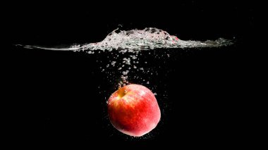 Kırmızı elma siyah arkaplanda suya düşüyor.