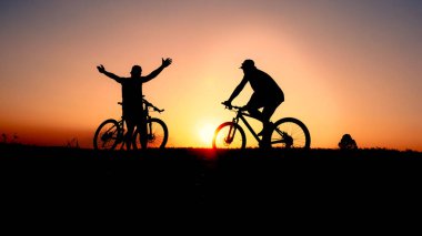 Günbatımının karanlık arka planında bisikletçi ve bisiklet siluetleri dolu
