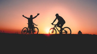 Günbatımının karanlık arka planında bisikletçi ve bisiklet siluetleri dolu
