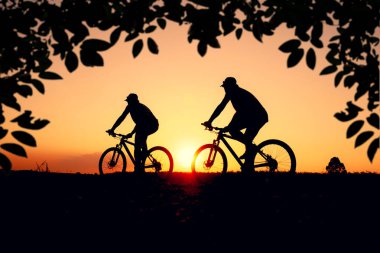 Günbatımının karanlık arka planında bisikletçi ve bisiklet siluetleri dolu