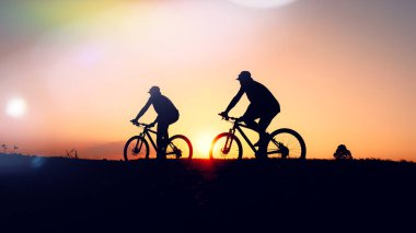Günbatımının karanlık arka planında bisikletçi ve bisiklet siluetleri dolu
