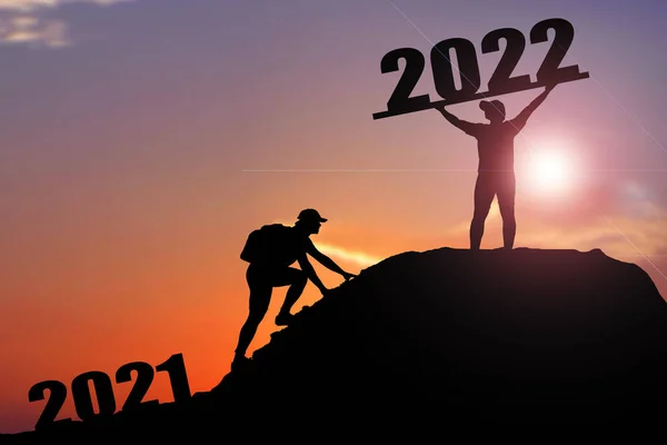 Welcome merry Christmas and happy new year in 2022,Silhouette Man from 2021cliff to 2022 cliff with cloud sky and sunlight. Man holding 2022 banner on top of mountain. Happy New Year 2022 concept.