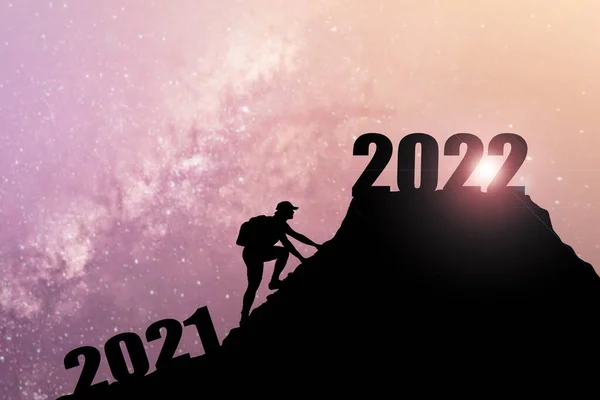 欢迎快乐的圣诞和快乐的新年在2022年 轮廓人从2021悬崖到2022悬崖与云天和阳光 男子举着2022年的旗帜在山顶上 祝2022年新年快乐 攀岩者在山顶发现2022年的标志 — 图库照片