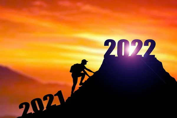 2022年の陽気なクリスマスと幸せな新年を歓迎し Silhouette Manは2021年の崖から2022年の崖まで雲の空と太陽の光で 男は山の上に2022年のバナーを保持 2022年の新年のコンセプト ロッククライミングマンは山の上に2022サインを見つける — ストック写真