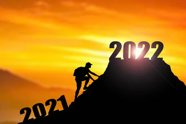 2022年の陽気なクリスマスと幸せな新年を歓迎し Silhouette Manは2021年の崖から2022年の崖まで雲の空と太陽の光で 男は山の上に2022年のバナーを保持 2022年の新年のコンセプト ロッククライミングマンは山の上に2022サインを見つける — ストック写真