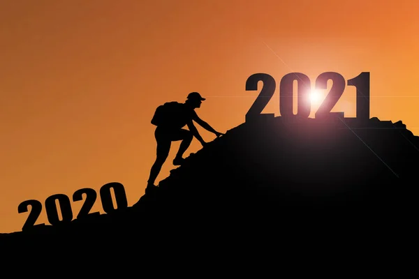 Welcome merry Christmas and happy new year in 2021,Silhouette Man from 2020cliff to 2021 cliff with cloud sky and sunlight. Man holding 2021 banner on top of mountain. Happy New Year 2021 concept.
