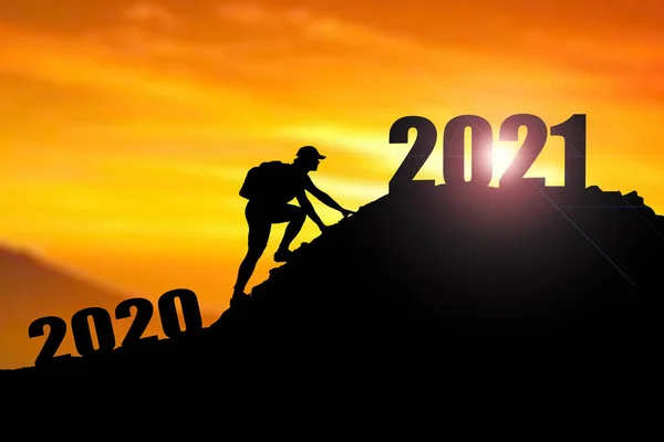 2021年の陽気なクリスマスと幸せな新年 2020年の崖から2021年の崖に雲の空と太陽の光でSilhouette男を歓迎します 山の上に2021年のバナーを持っている男 ハッピーニューイヤー2021のコンセプト — ストック写真