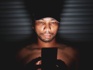 Asyalı bir adam evini özleyen karanlık bir köşede cep telefonuna bakar..